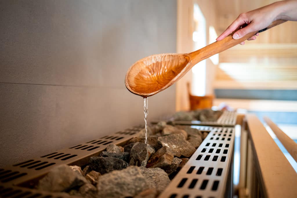 Pouring water on hot stone into heater in sauna